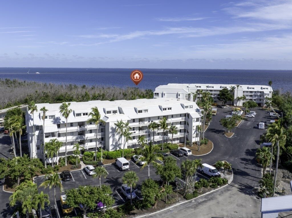 A multi-story hotel with a parking lot, surrounded by palm trees and a view of the ocean.