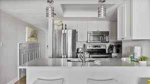 Une cuisine moderne dotée d’appareils électroménagers en acier inoxydable, d’un îlot central avec des tabourets de bar et de meubles de rangement blancs.