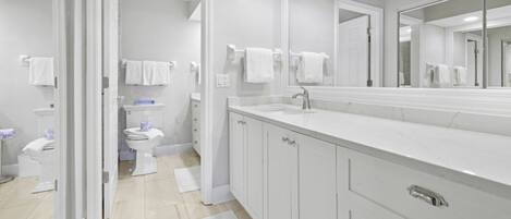 Un baño moderno con un espejo grande, muebles blancos y un inodoro visible al fondo.