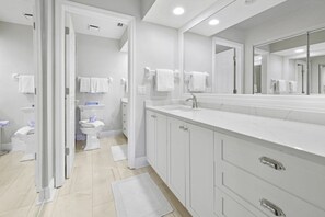 Ein modernes Badezimmer mit großem Spiegel, weißen Schränken und einer Toilette im Hintergrund.