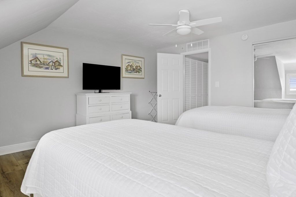 Un dormitorio con cama, televisor, cómoda y ventilador de techo.