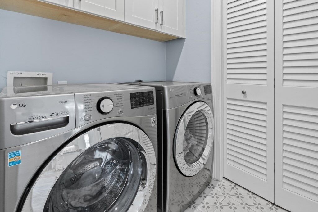 Un espace buanderie équipé de deux machines à laver LG à entraînement direct, d’un meuble de rangement au-dessus et d’une porte blanche à panneaux ajourés.