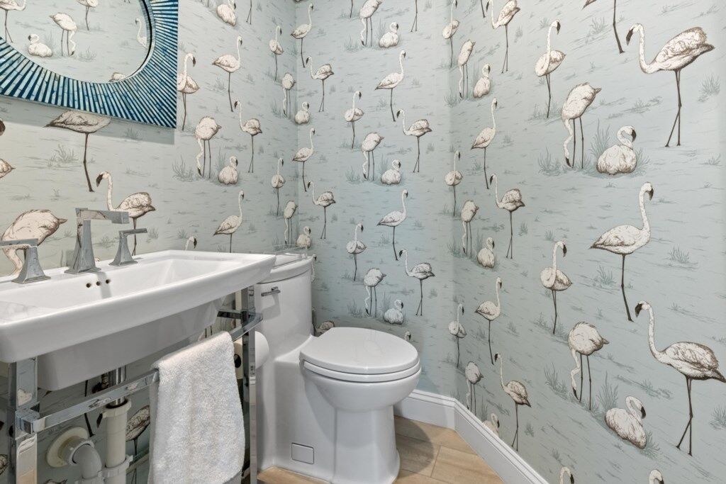 Ein Badezimmer mit Toilette, Waschbecken und Spiegel. Die Wände sind mit einem Flamingomotiv verziert.