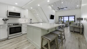 A modern kitchen with white cabinetry, a large island with stools, a built-in oven, and a ceiling fan. - South Seas Beach Villa 2535 4 Bedroom Home by RedAwning (Captiva)