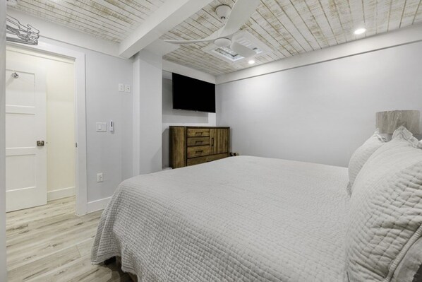 A bedroom with a bed, wooden dresser, and a mounted TV.