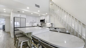 A modern kitchen with white cabinetry, a large island, and a staircase with white railings. - South Seas Beach Villa 2535 4 Bedroom Home by RedAwning (Captiva)