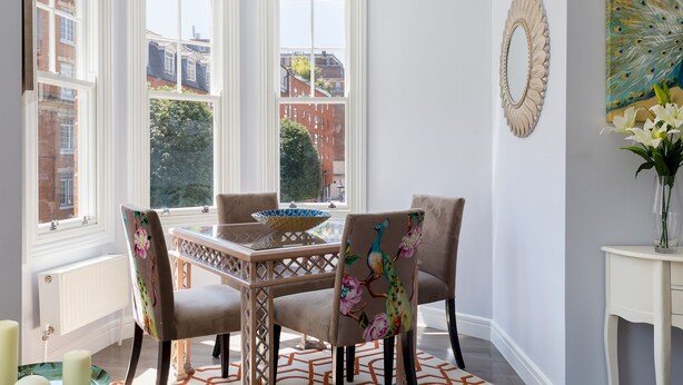 A dining area with a table, chairs, and a peacock-themed chair.