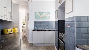 A narrow kitchen with white cabinets, a blue backsplash, and a small island with a sink.
