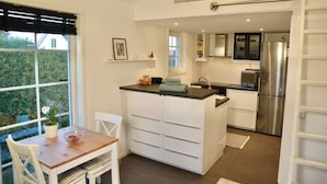 A compact kitchen with a central island, a dining area with a table and chairs, and a view of the outdoors through a large window. - Private mini-villa with patio (Katrineholm)