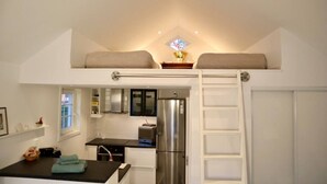 A compact kitchen with a built-in refrigerator, a dining area with a table and chairs, and a loft bedroom with a ladder. - Private mini-villa with patio (Katrineholm)