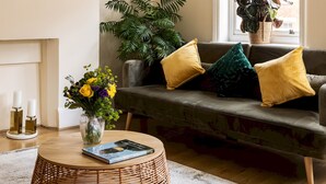 A living room with a sofa, a round coffee table, a clock, and a window with a plant. - One Bedroom Apartment in Marylebone (London)