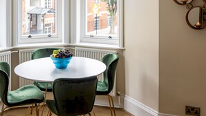 A dining area with a round table, green chairs, and a bowl of fruit. - One Bedroom Apartment in Marylebone (London)