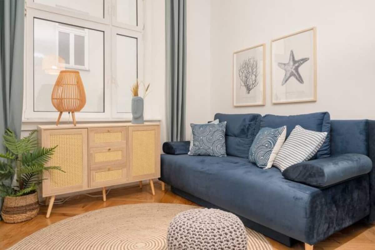 A modern living room with a blue sofa, a rattan cabinet, and a round rug.