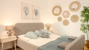 A neatly arranged bedroom with a bed, two bedside tables, a wall-mounted mirror, and framed botanical illustrations. - Designer Apartment - 5 min to Center (Vienna)