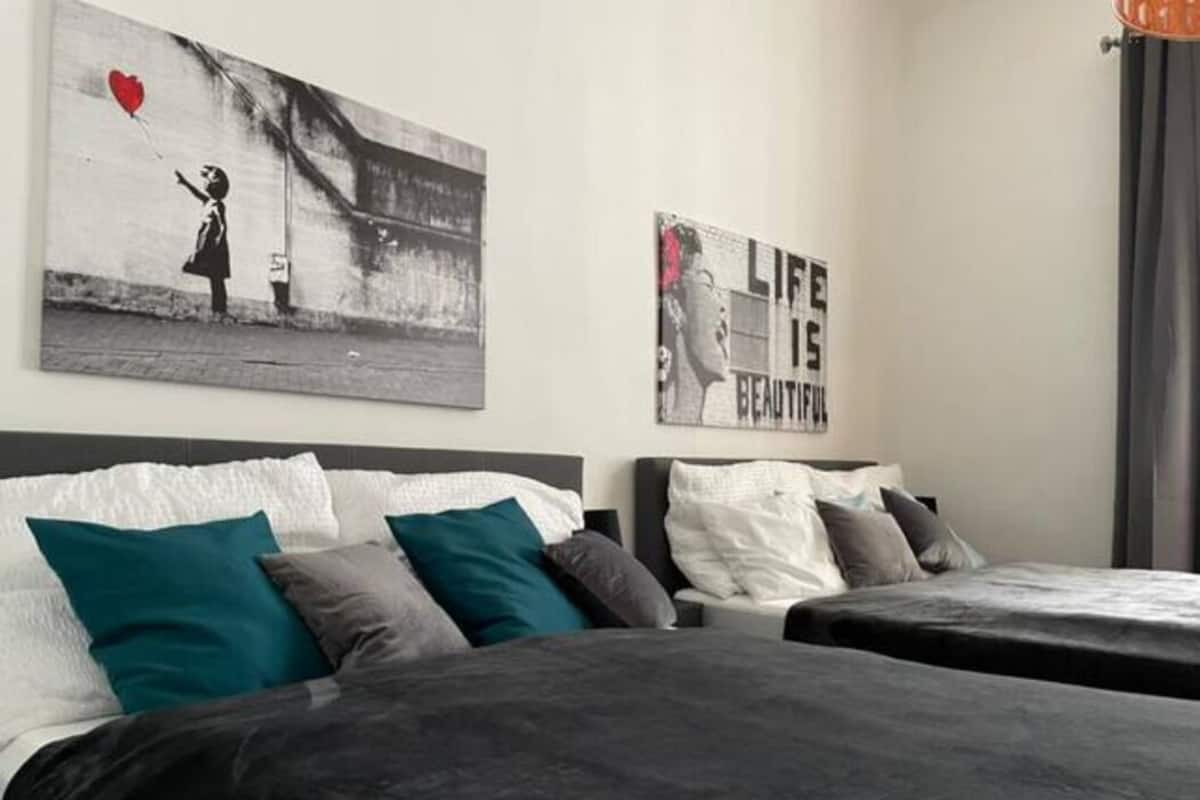 A hotel room with two beds, teal and grey pillows, and two wall art pieces.