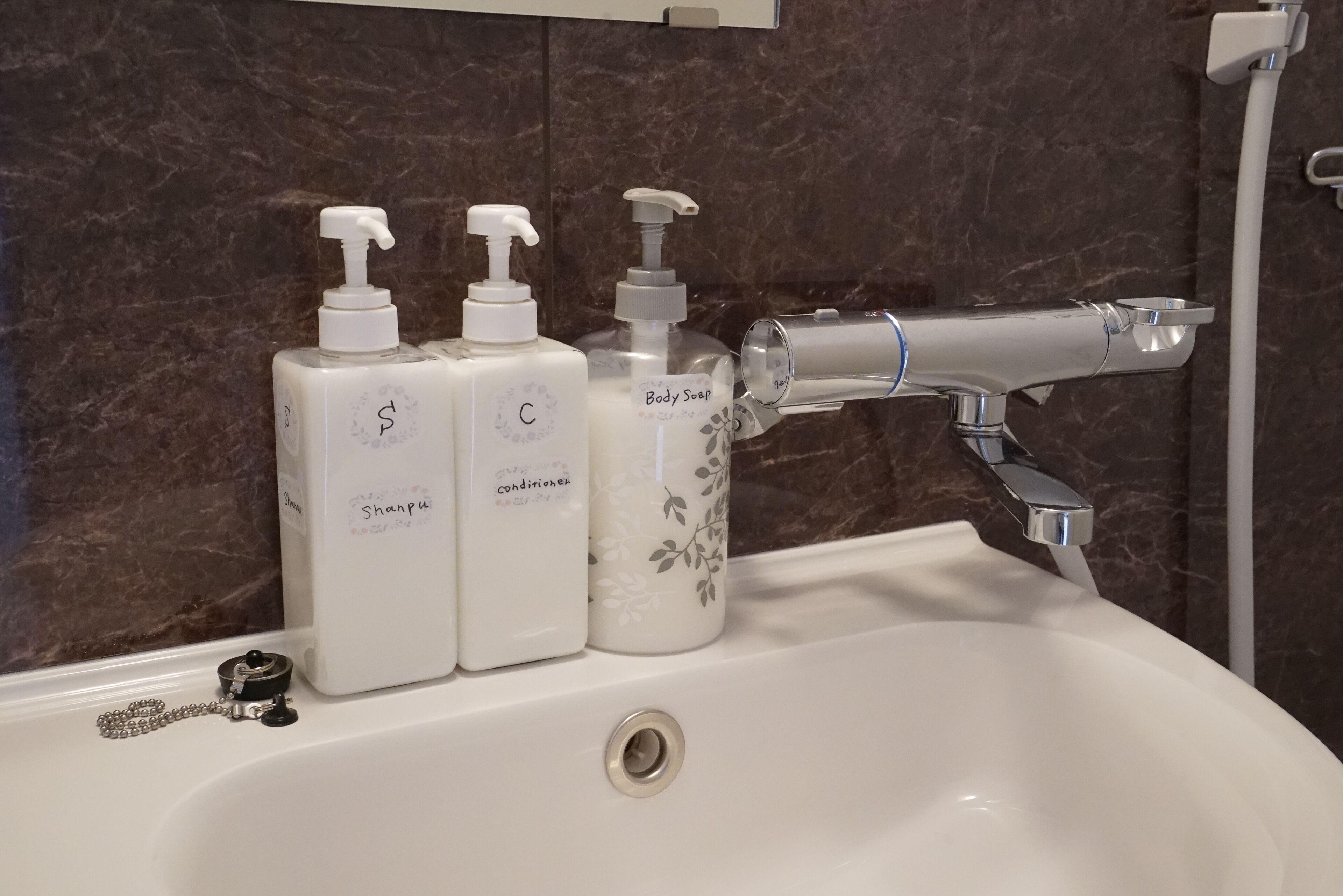 A bathroom sink with three bottles of liquid soap labeled "Shampoo," "Conditioner," and "Body Soap."