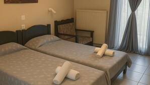 Ein Hotelzimmer mit zwei Betten, einem Nachttisch, einem Sessel, einem Gemälde und einem Fenster mit Vorhängen.
