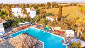 Ein Poolbereich mit Liegestühlen und Sonnenschirmen, umgeben von Gebäuden und mit Blick ins Grüne.