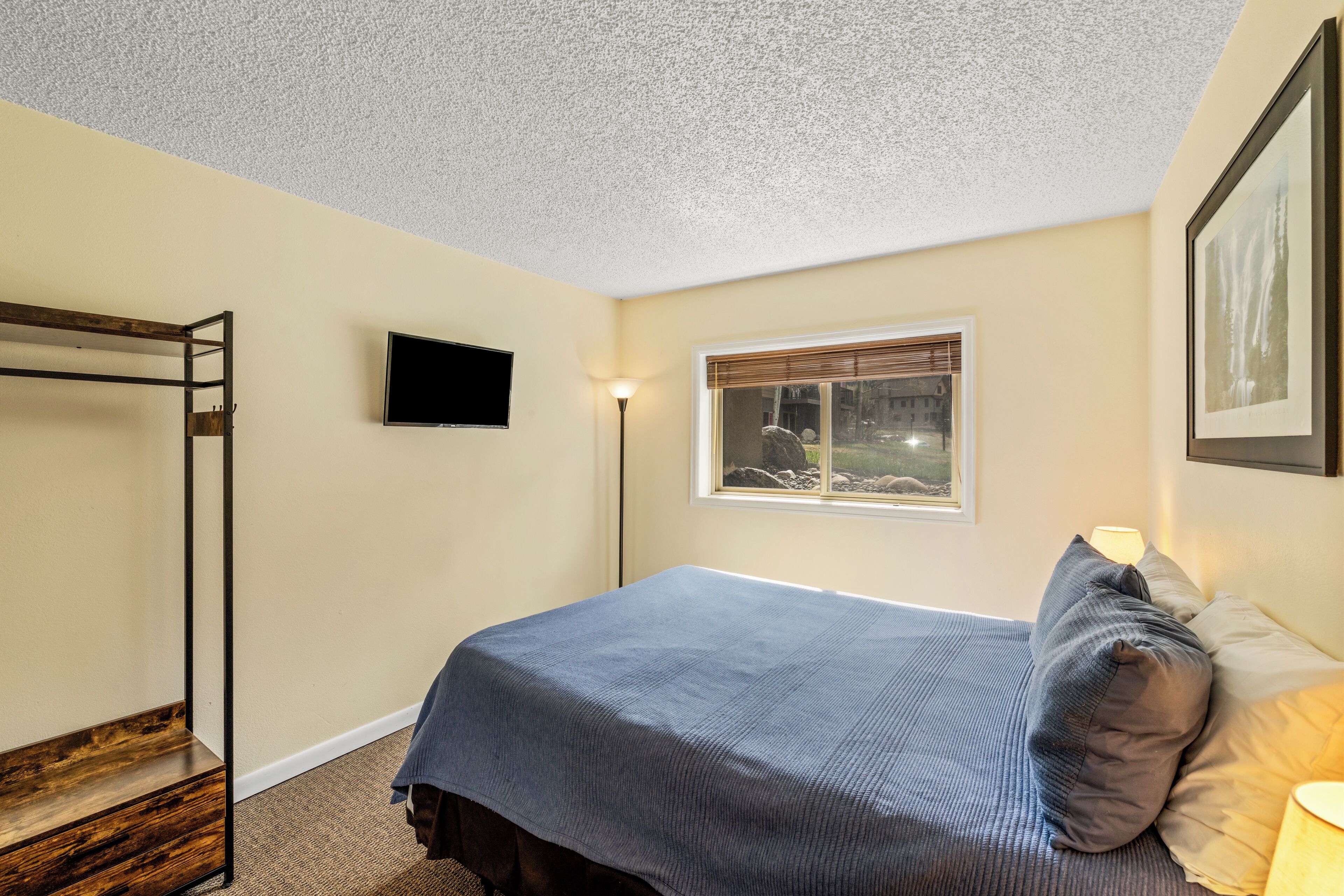 A bedroom with a bed, a TV, a window, and a lamp.
