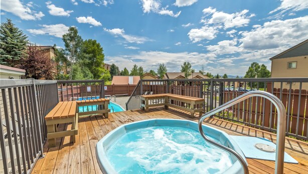 Une terrasse en bois avec un jacuzzi, une piscine et une clôture en bois.