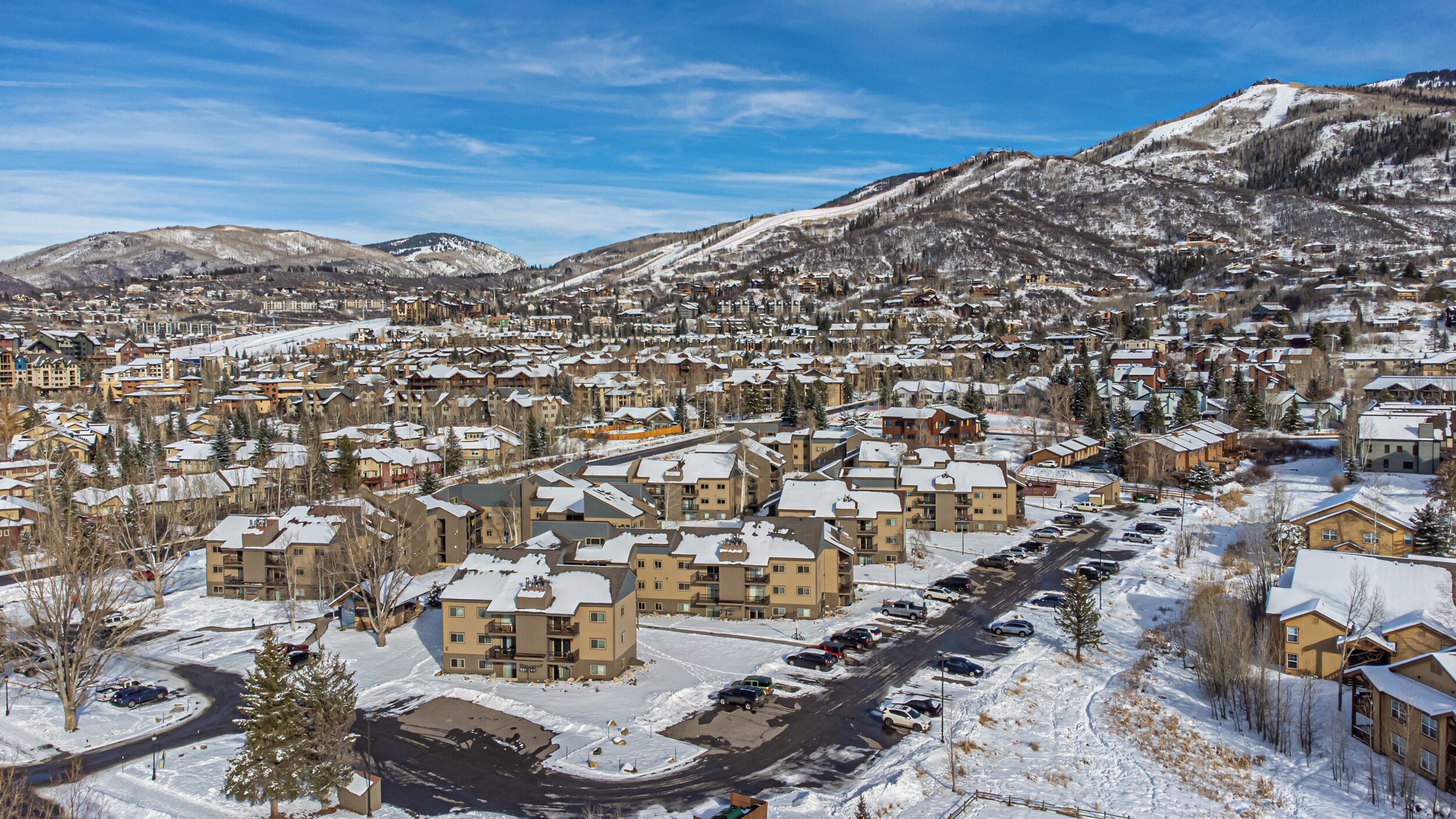 A residential area with snow-covered buildings, a main road, and mountains in the background.