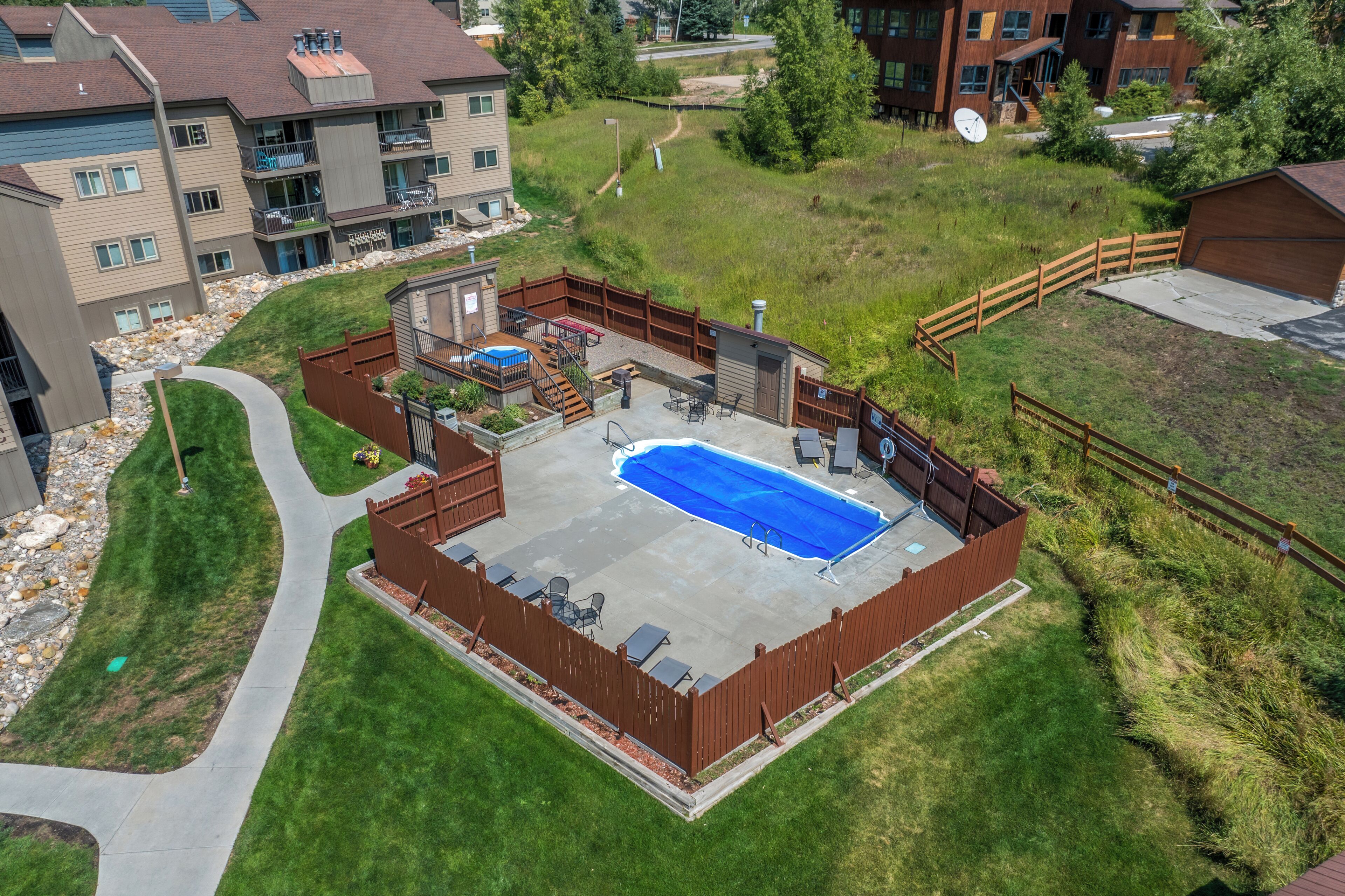 A residential complex with a swimming pool, outdoor seating, and a fenced yard.