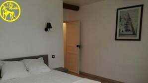 A bedroom with a bed, a nightstand, a wall-mounted lamp, a door, and a framed picture on the wall. - Chez Makita - RdC (Mirepeisset)