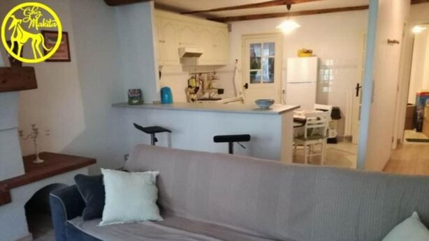 A living room with a sofa, a small table, and a kitchen area in the background. - Chez Makita - RdC (Mirepeisset)