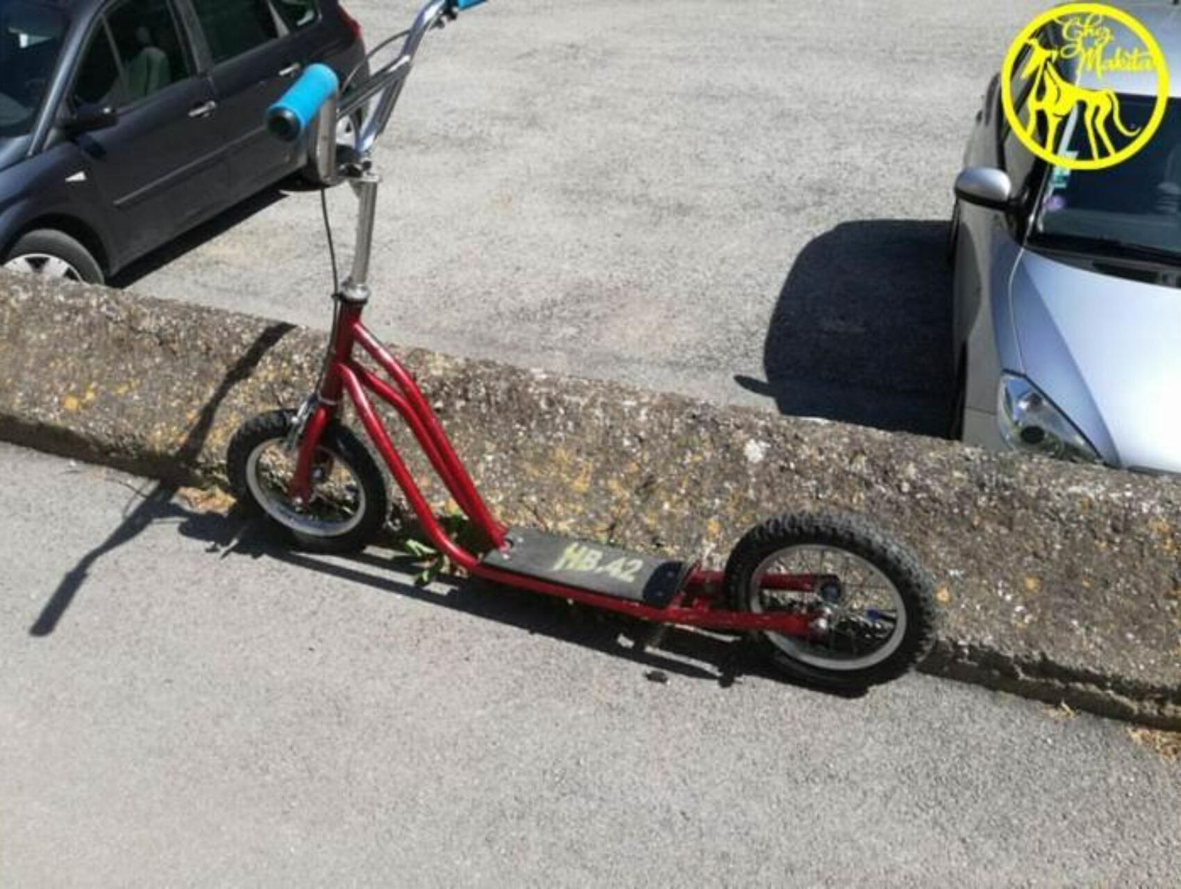 Ein roter Elektroroller steht auf einem Betonbord neben einem Auto.