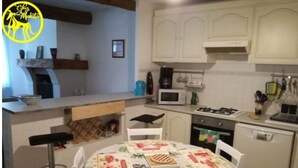 A compact kitchen with white cabinets, a microwave, a gas stove, and a small refrigerator. - Chez Makita - RdC (Mirepeisset)