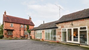 A two-story brick house with a garage, a driveway, and a garden area with potted plants. - Abbey View Farm Cottage (Uttoxeter)