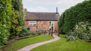 A brick house with a paved garden path leading to a patio area with outdoor furniture. - Abbey View Farm Cottage (Uttoxeter)