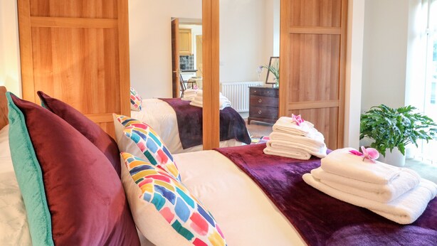A bedroom with a bed, pillows, a bedside table, a mirror, and a window. - Abbey View Farm Cottage (Uttoxeter)