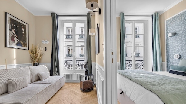 Una habitación de hotel moderna con sofá, cama, vistas a la ciudad y una ventana con cortinas.