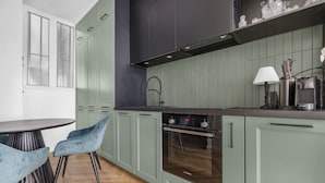 Una cocina con armarios verdes, un horno Bosch, una campana extractora negra y una zona de comedor con una mesa redonda y sillas azules.