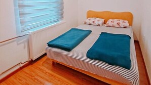 Una habitación pequeña y limpia con una cama individual, un radiador y una ventana con persianas.