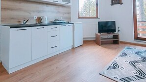 Una cocina moderna con armarios blancos, una encimera de madera, una tetera y un televisor sobre un mueble de madera.