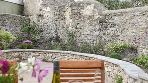 An outdoor dining area with stone walls, a wooden bench, and a table set for two with plates, glasses, and a bottle. - Malabar House (Lyme Regis)