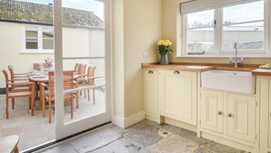 A kitchen with a large window, a dining area with wooden furniture, and a stone floor. - Malabar House (Lyme Regis)