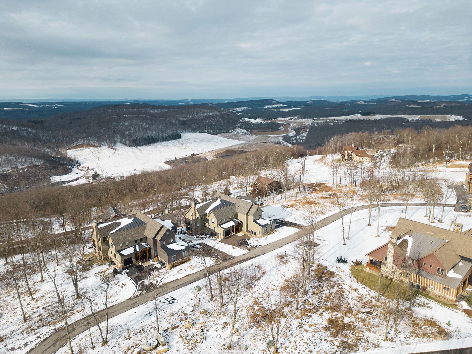 A residential area with multiple houses, a winding road, and a snowy landscape.
