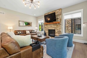 A living room with a stone fireplace, leather sofa, blue armchairs, and a flat-screen TV mounted above the fireplace.