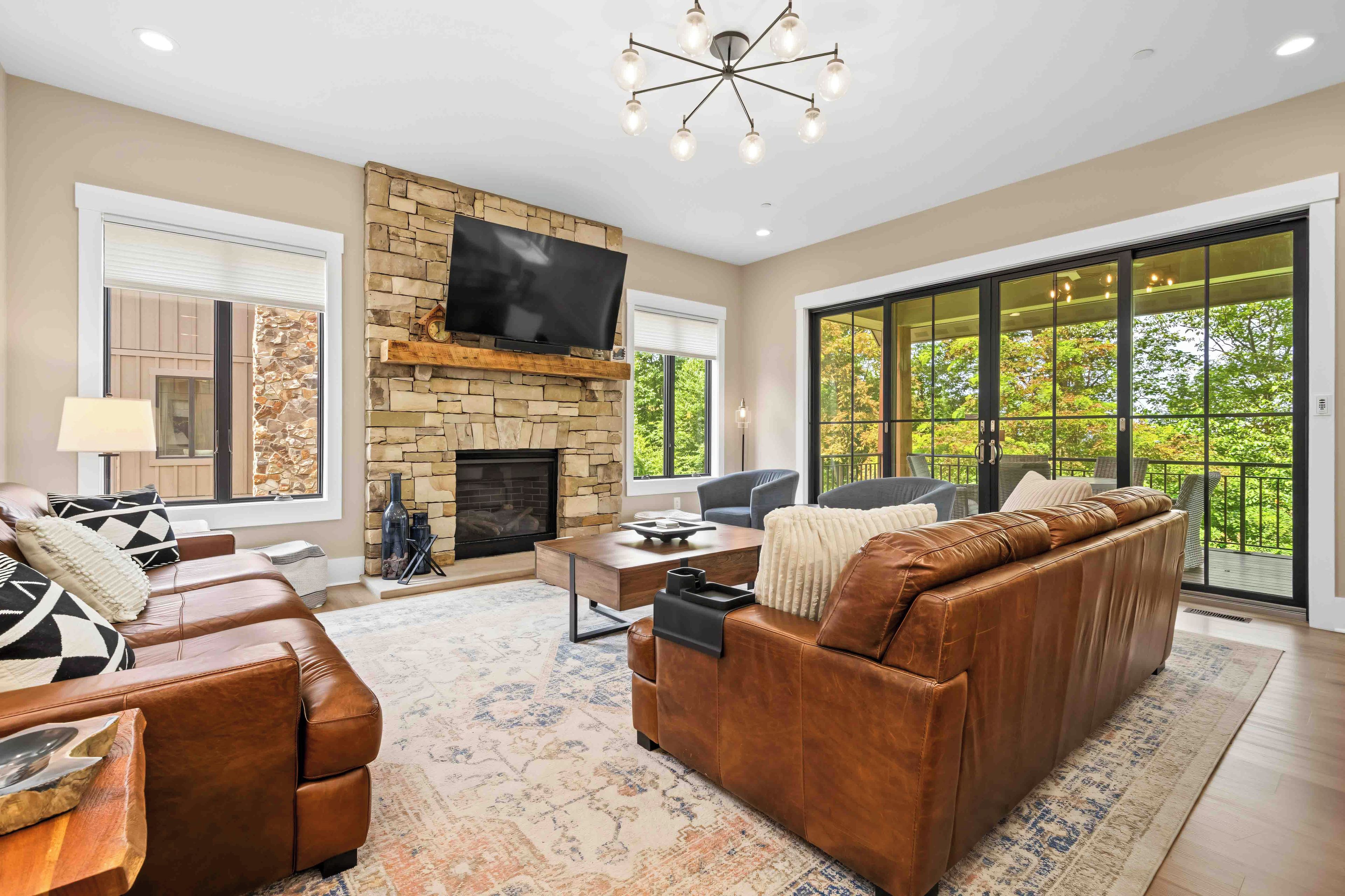 A living room with a stone fireplace, leather sofa, and a large TV.