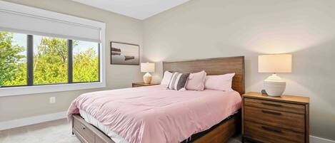 A bedroom with a bed, nightstands, a ceiling fan, and a window with a view of trees.