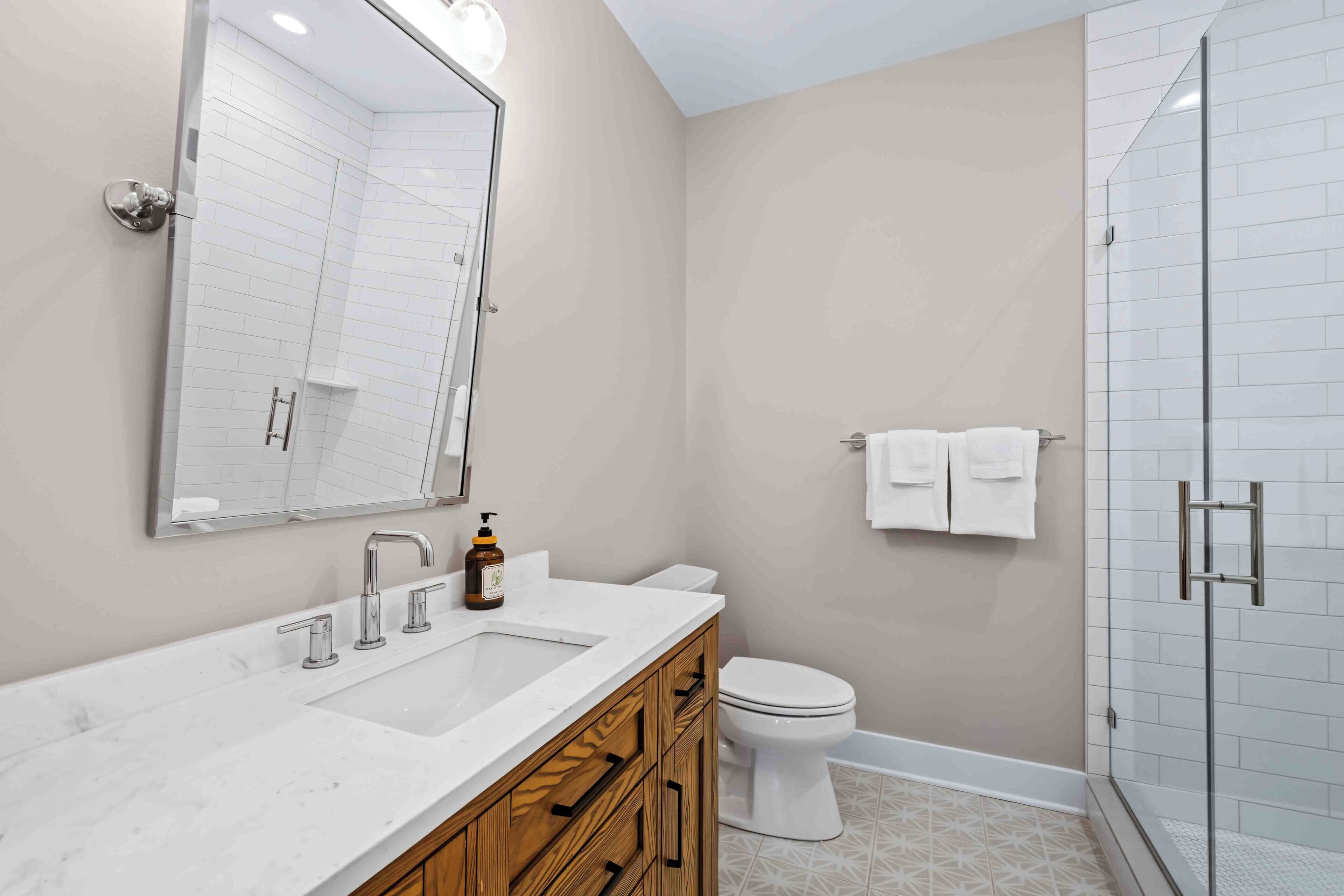 A modern bathroom with a white vanity, a large mirror, a toilet, and a shower area.