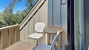 A wooden deck with two chairs and a small round table, overlooking a clear blue sky and trees.