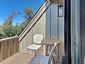 A wooden deck with two chairs and a small round table, overlooking a clear blue sky and trees. - Mountain Mindset by Taylor Made Deep Creek (McHenry)