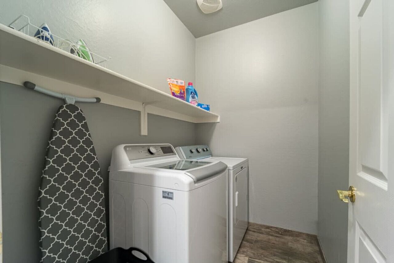 Une buanderie équipée d’un lave-linge et d’un sèche-linge, d’un étendoir et d’étagères contenant des produits de lessive.