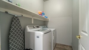 A laundry room with a washing machine and dryer, a drying rack, and shelves with laundry supplies. - Bella Bella!  Heated Pool/HotTub/Sauna/BBQ (Casa Grande)