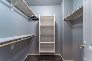 Ein begehbarer Kleiderschrank mit weißem Regalsystem und Kleiderstange.