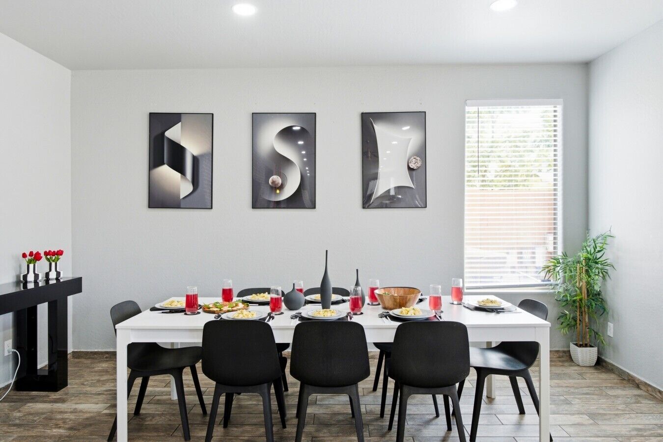 Uma sala de jantar com uma mesa branca posta para quatro pessoas, cadeiras pretas e arte abstrata na parede.